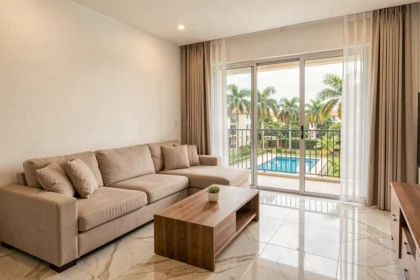 Salon moderne d'un appartement en résidence à Abidjan avec balcon donnant sur une piscine et des palmiers